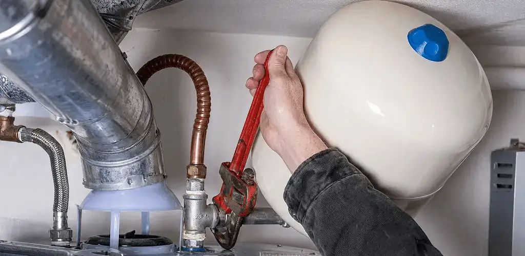 Water heater repair technician tightening plumbing connections near a tank unit in Scottsdale, AZ